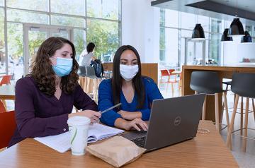 Two face masked female students working together inside Benson Center